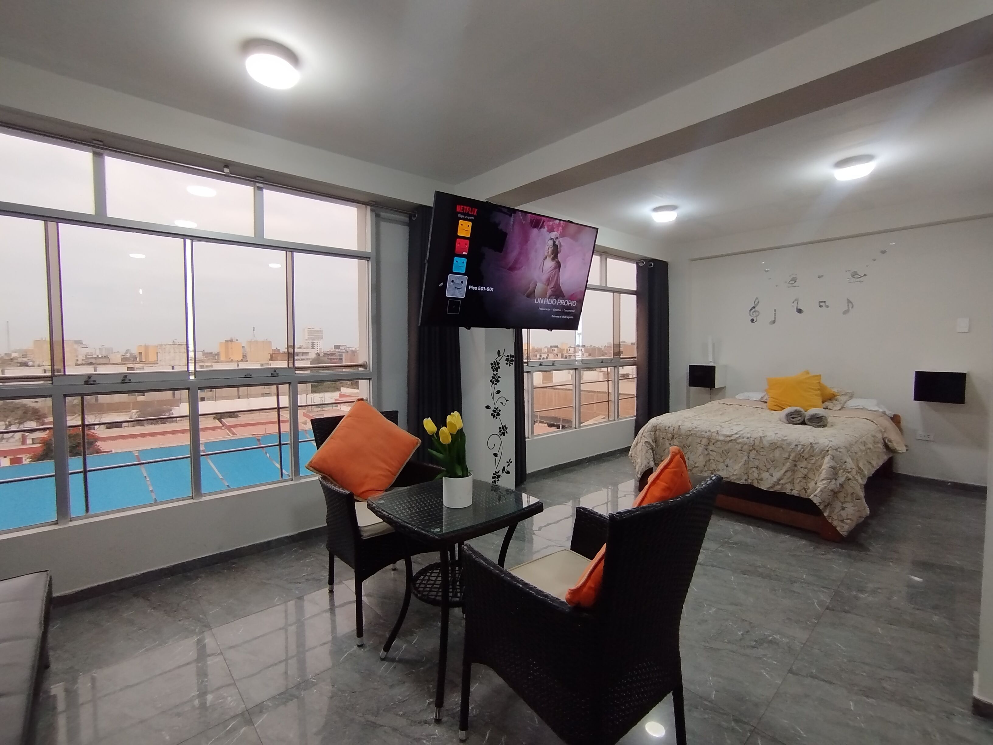 Habitación de hotel con cama, televisión, mesa de comedor con sillas y vista a una piscina.