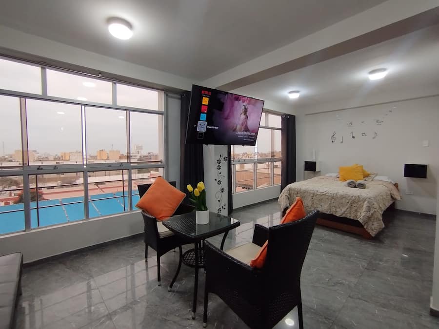 A hotel room with a bed, a TV, a dining table with chairs, and a view of a swimming pool.