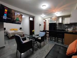 Ein modernes Wohnzimmer mit Flachbildfernseher, einer Couch, einem Esstisch mit Stühlen, einer Küchenzeile und einem Flur.