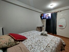A hotel room with a bed, a TV mounted on the wall, a small table, and a mirror on the wall.