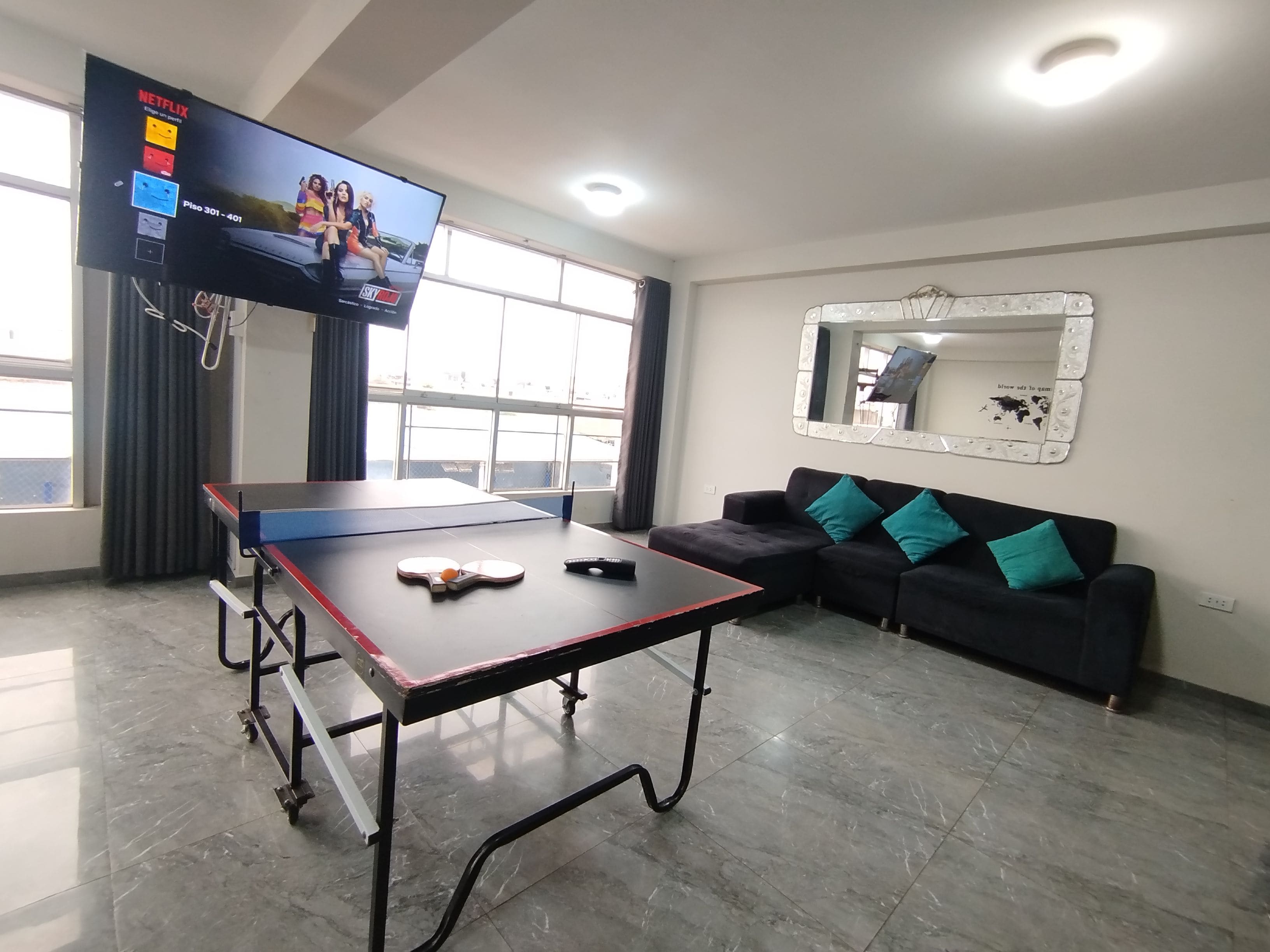 Habitació amb taula de ping-pong, sofà, televisió i una finestra gran.