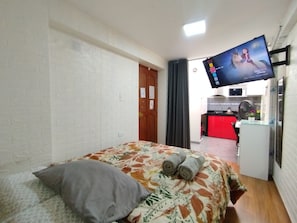 A hotel room with a bed, a flat-screen TV mounted on the wall, a kitchenette in the background, and a door leading to another room. - Departamentos Appart d'Eliette (Trujillo)