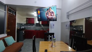 Un espacio habitable compacto con kitchenette, una zona de comedor con mesa y sillas, y un televisor montado en la pared.