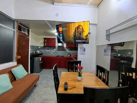 Un espacio habitable compacto con un sofá, una mesa de comedor con sillas, un televisor en la pared y una kitchenette al fondo.