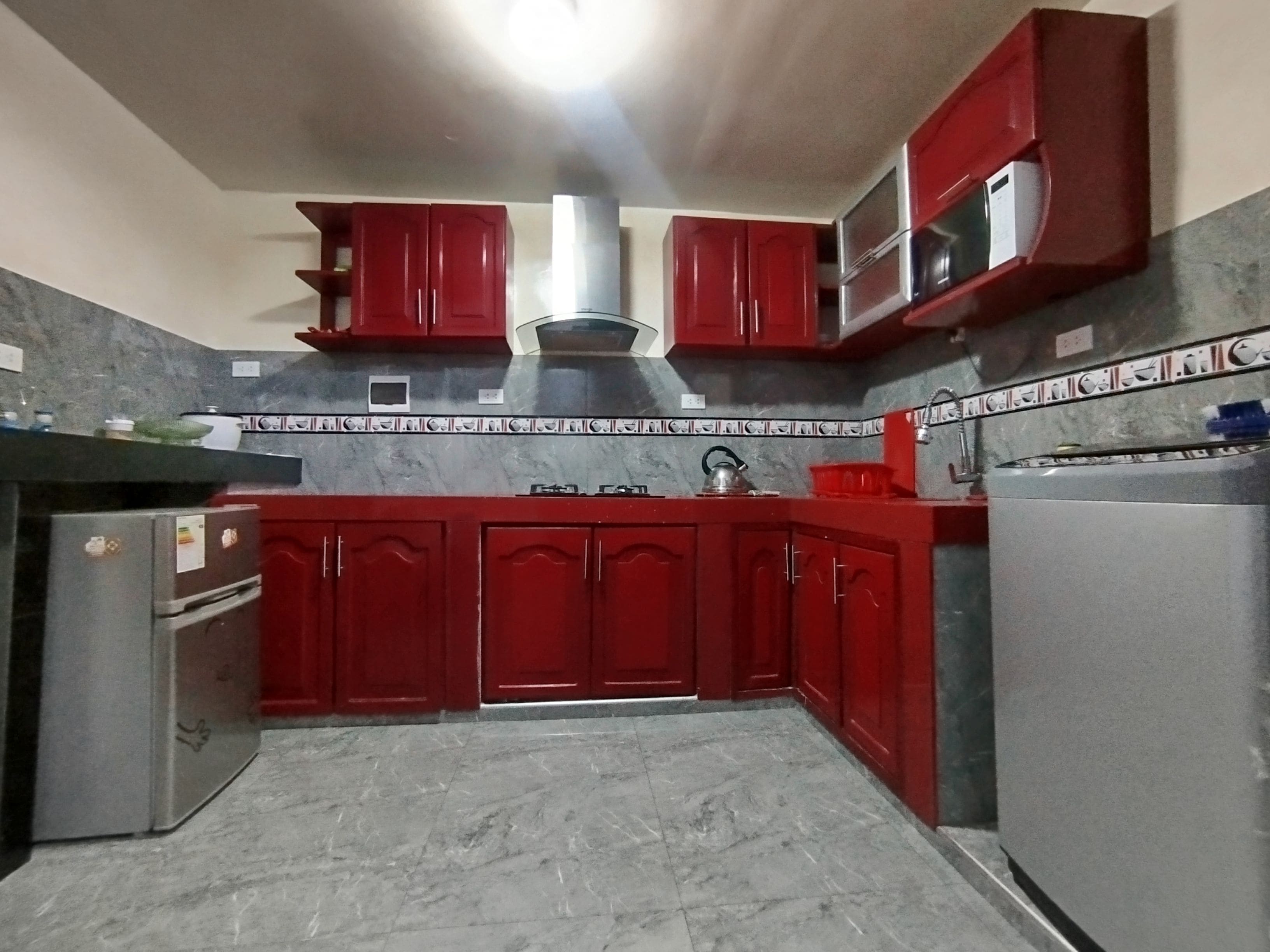 A kitchen with red cabinets, a stainless steel range hood, and a marble countertop.