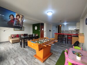 A living room with a foosball table, a television mounted on the wall, and a kitchen area in the background. - Departamentos Appart d'Eliette (Trujillo)