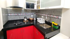 A compact kitchen with a gas stove, a kettle, a sink, and a microwave. - Departamentos Appart d'Eliette (Trujillo)