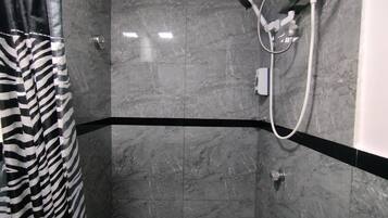 Área de chuveiro com cortina listrada preta e branca, chuveiro manual e painel de controle fixado na parede.