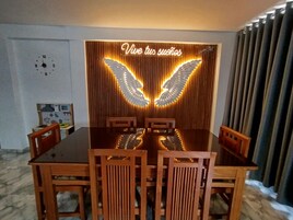 Un comedor con una mesa y sillas de madera, un letrero de neón con alas y un reloj en la pared.