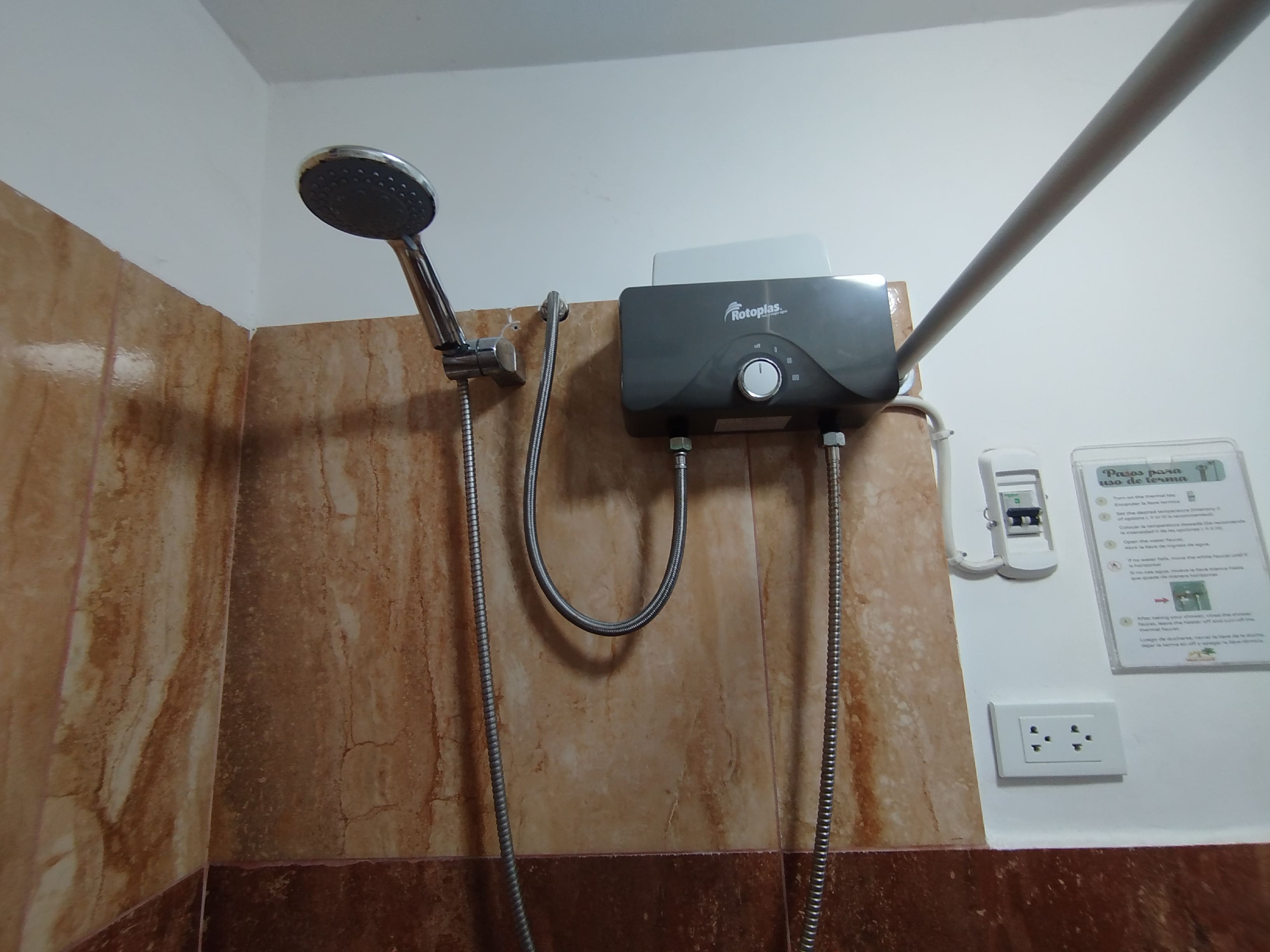 Um banheiro com chuveiro, painel de controle na parede e tomada.
