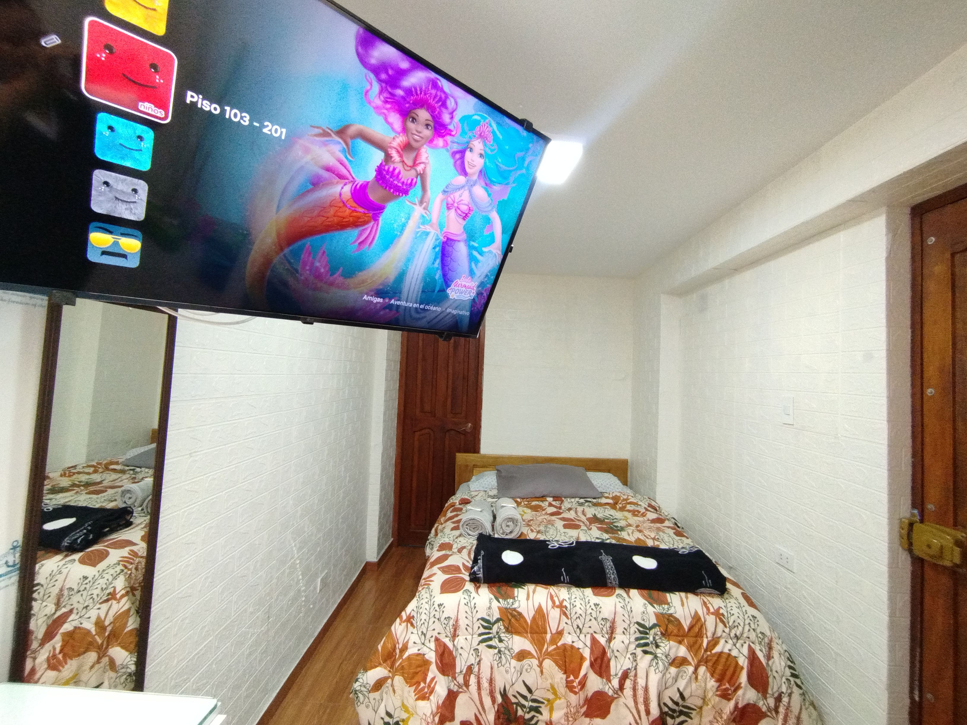 A room with a bed, a television mounted on the wall, and a door.