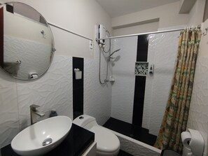 Uma casa de banho com uma sanita, um lavatório branco e um chuveiro com parede em azulejos a preto e branco, além de um espelho sobre o lavatório.