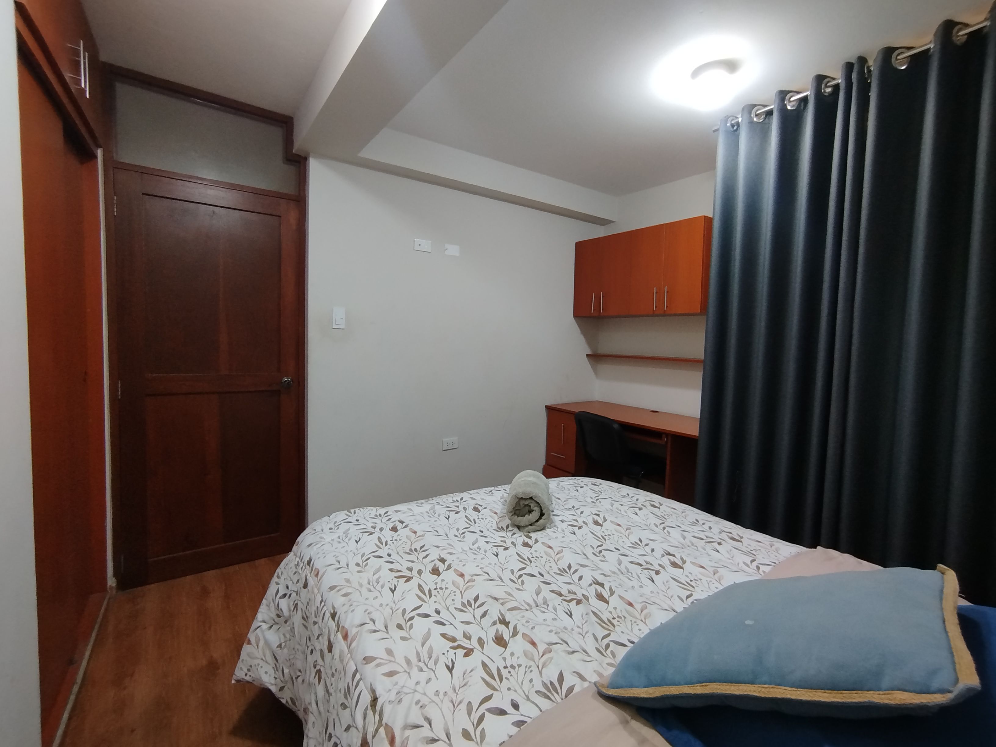 A bedroom with a bed, a desk, a wardrobe, and a curtain.