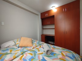 Un dormitorio con una cama, un almohadón, una toalla enrollada y un armario con varios estantes.