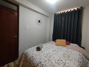 A bedroom with a bed, a wall clock, a door, and curtains. - Departamentos Appart d'Eliette (Trujillo)