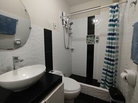 Un baño con un lavamanos blanco, un inodoro, una ducha con cortina a rayas y un espejo en la pared.