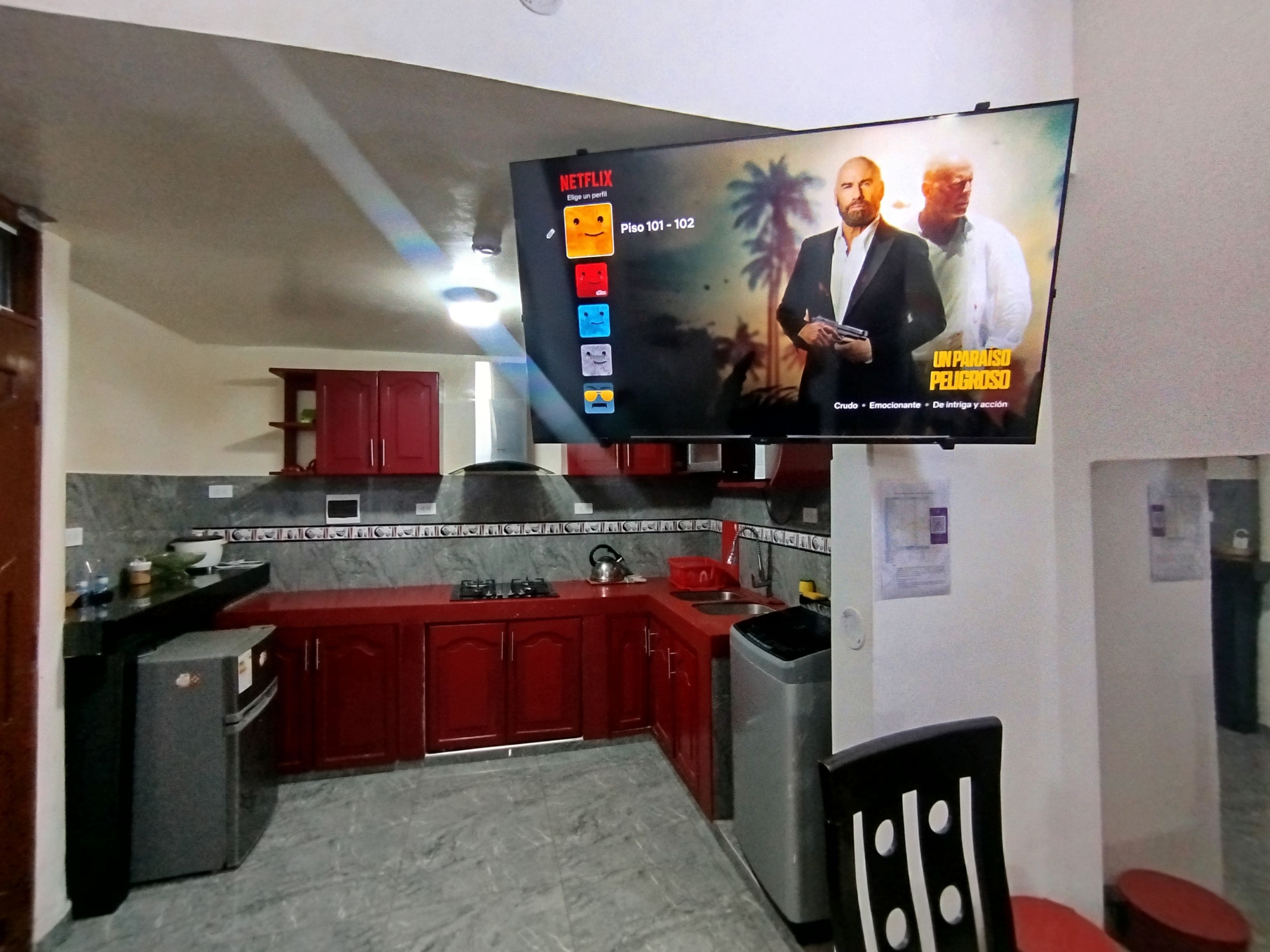 A kitchen with a TV mounted on the wall displaying a Netflix interface.