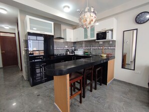 A modern kitchen with a black countertop island, wooden stools, a microwave, and a hanging light fixture. - Departamentos Appart d'Eliette (Trujillo)