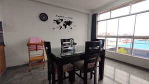 A dining area with a glass table, four chairs, a world map on the wall, a clock, and a window with a view. - Departamentos Appart d'Eliette (Trujillo)