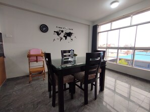 A dining area with a glass table, four chairs, a world map on the wall, a clock, and a window with a view. - Departamentos Appart d'Eliette (Trujillo)