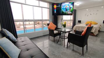 Een hotelkamer met een groot raam, een bank, een eettafel en een televisie.