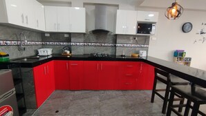 A kitchen with red cabinets, a black countertop, a stainless steel kettle, a microwave, and a clock on the wall. - Departamentos Appart d'Eliette (Trujillo)
