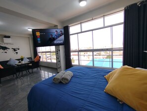 Habitación de hotel con una cama grande, un escritorio, un televisor y vistas amplias de la ciudad.