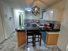 Una cocina moderna con piso de mármol, una isla central con taburetes y una lámpara colgante.