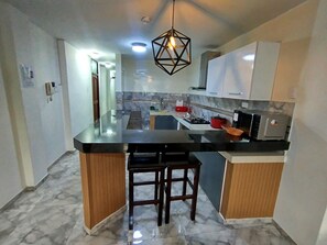 A modern kitchen with a marble floor, a central island with stools, and a hanging light fixture. - Departamentos Appart d'Eliette (Trujillo)