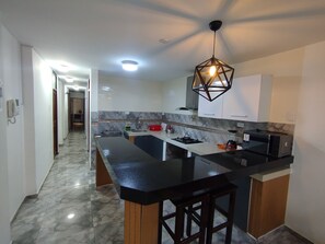 A modern kitchen with a marble backsplash, a black countertop, and a geometric pendant light.