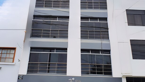 A multi-story building with a modern design, featuring a prominent vertical column, large windows, and a blue garage door. - Departamentos Appart d'Eliette (Trujillo)