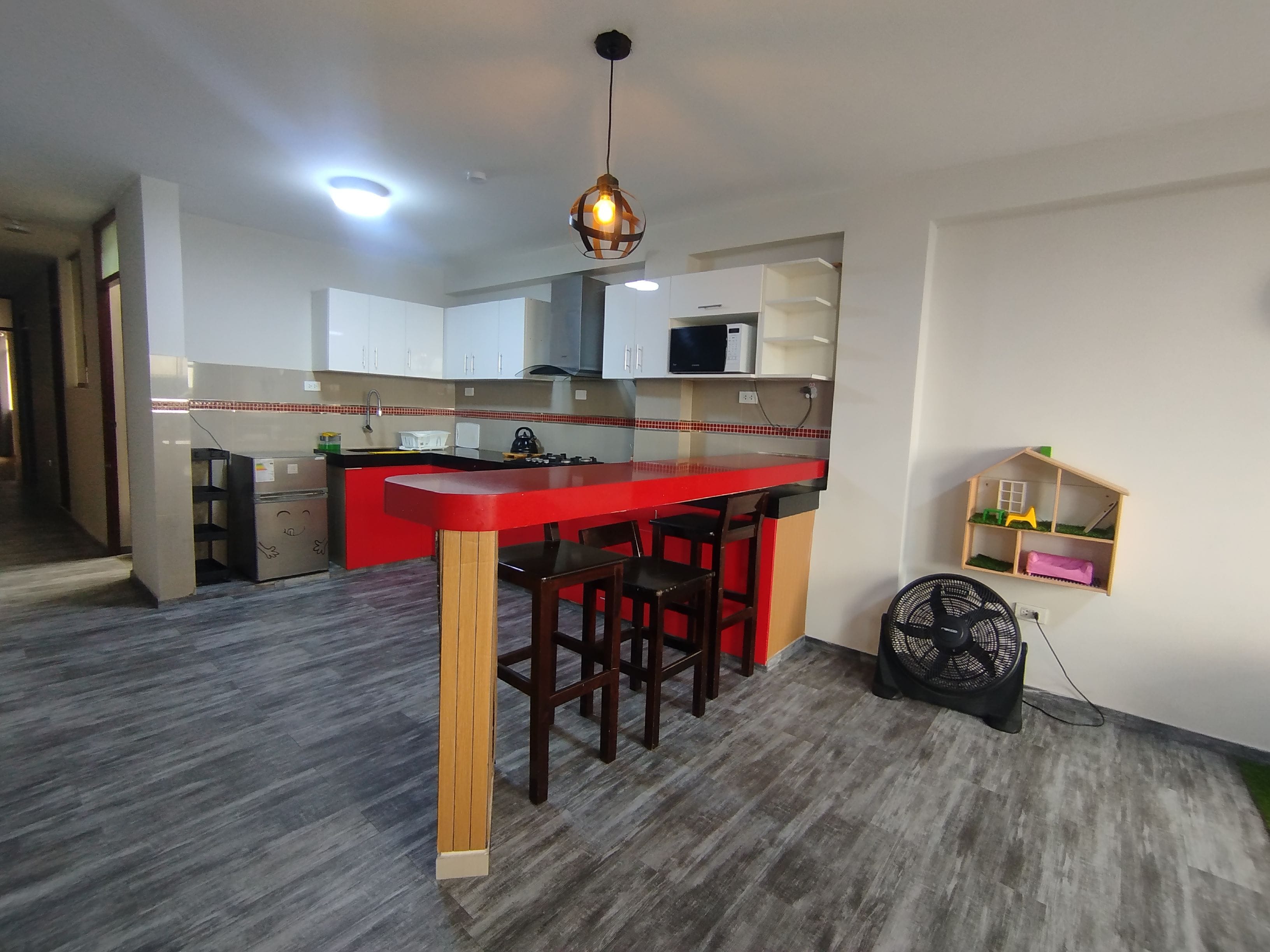 A kitchen with a red countertop, wooden stools, a microwave, and a fan.