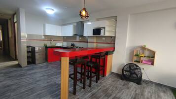 A kitchen with a red countertop, wooden stools, a microwave, and a fan.