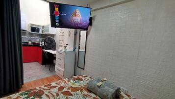 A hotel room with a bed, a desk, a television mounted on the wall, and a small kitchenette area.