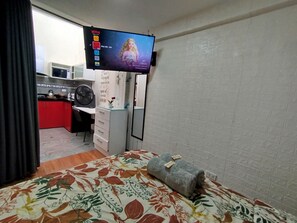 A hotel room with a bed, a desk, a television mounted on the wall, and a small kitchenette area. - Departamentos Appart d'Eliette (Trujillo)
