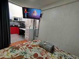 Habitación de hotel con cama, escritorio, televisor montado en la pared y una pequeña zona de kitchenette.