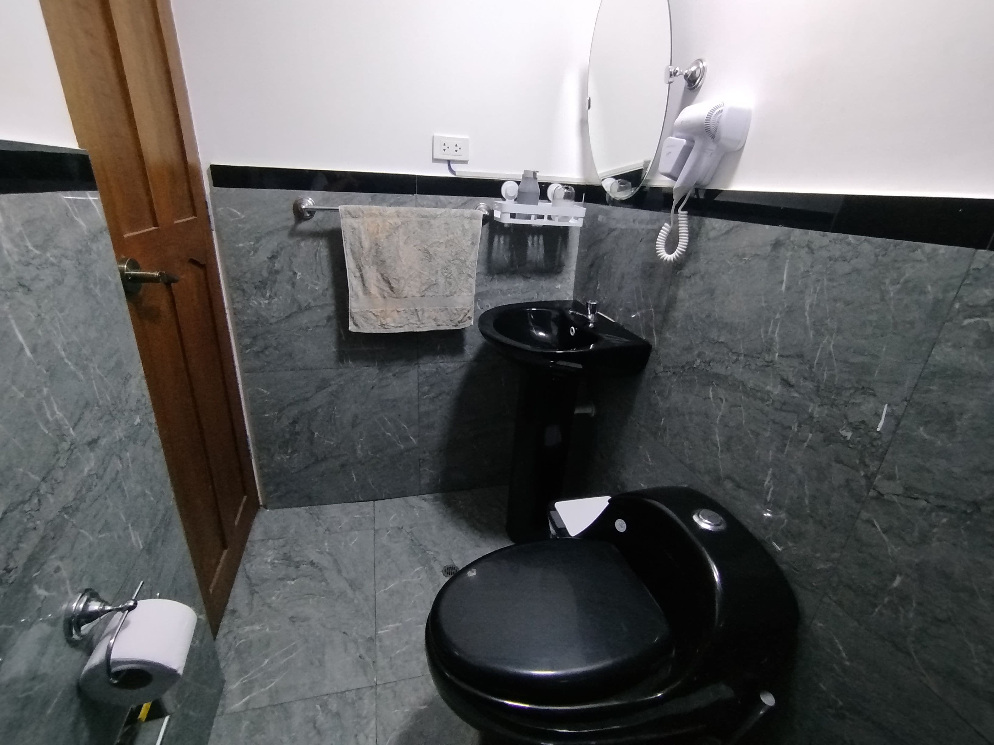 Een badkamer met een zwart toilet, een wastafel, een handdoekhouder en een haardroger.