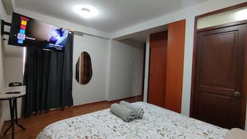 Habitación de hotel con una cama, un televisor en la pared, una mesita y una puerta.