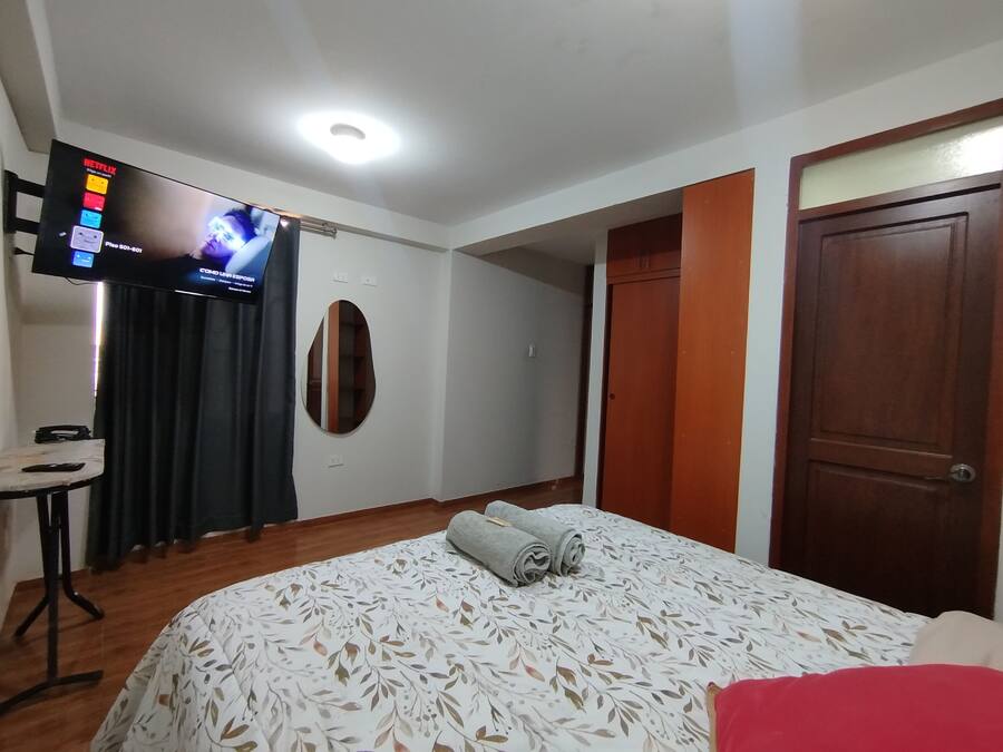 Habitación de hotel con una cama, un televisor en la pared, una mesita y una puerta.
