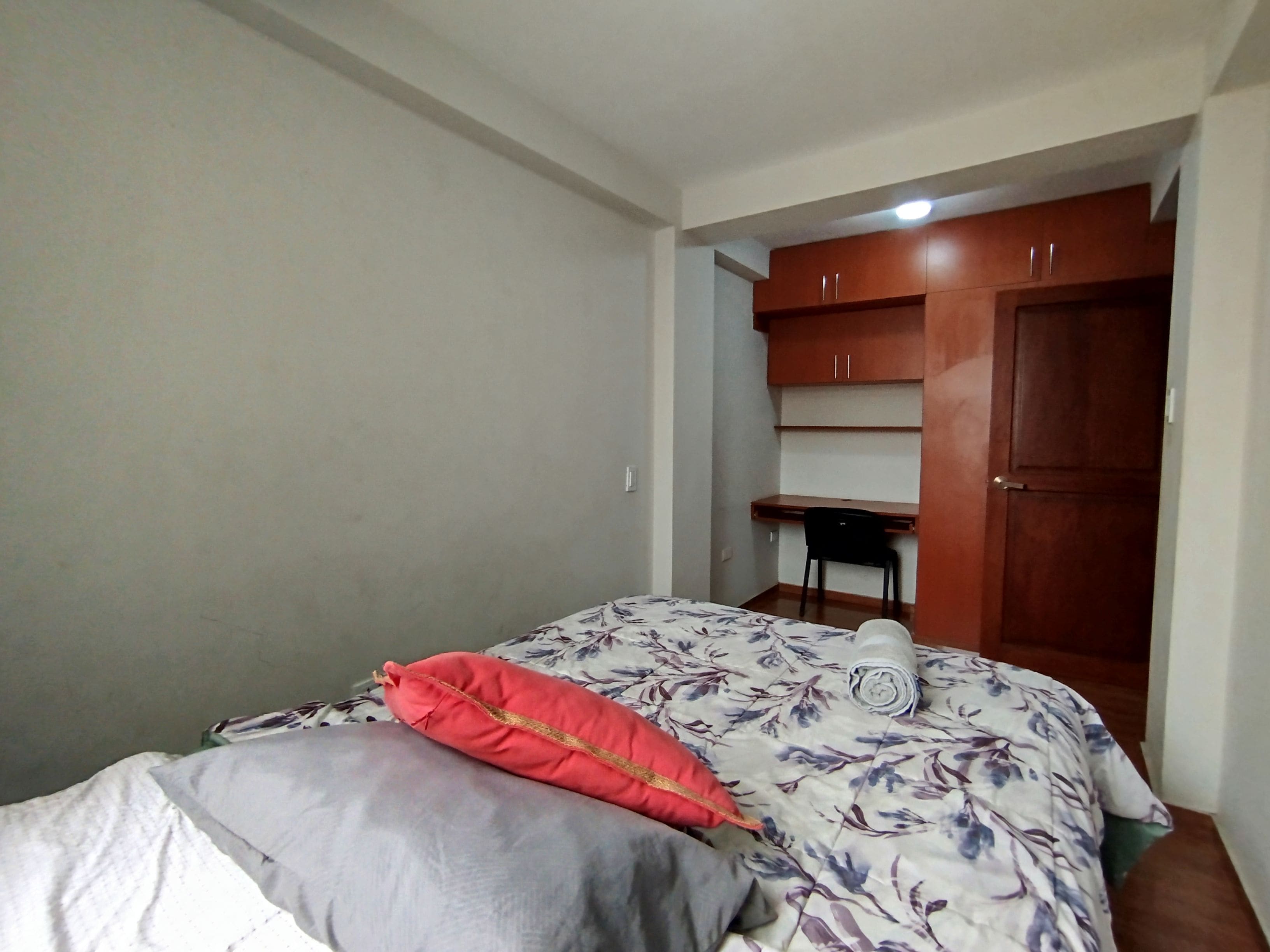 A bedroom with a bed, a desk, and a wardrobe.