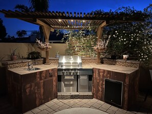An outdoor kitchen with a built-in grill, sink, and a pergola overhead.