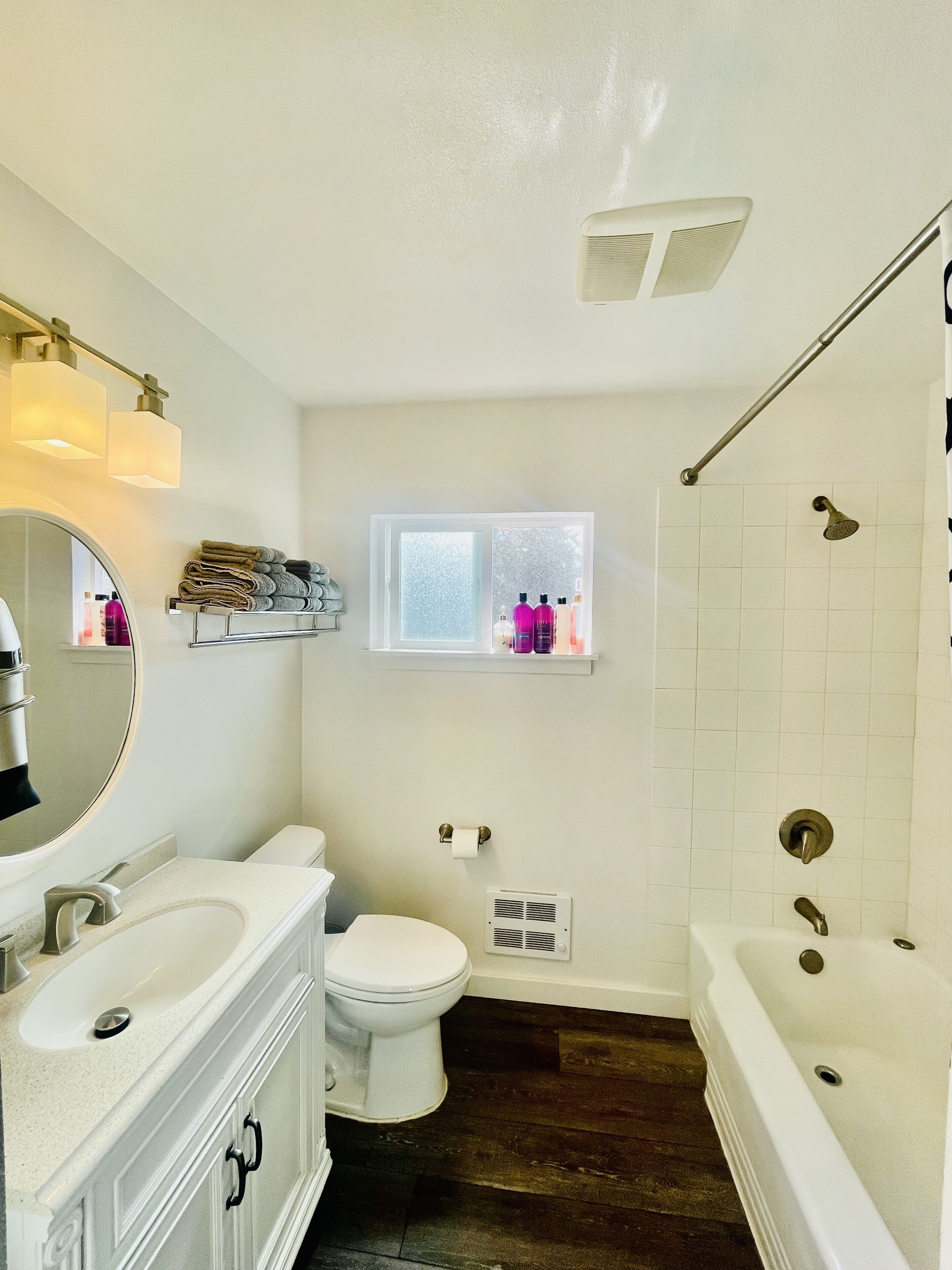 A bathroom with a toilet, sink, and bathtub. There is a window with a view of trees and a shelf with toiletries.