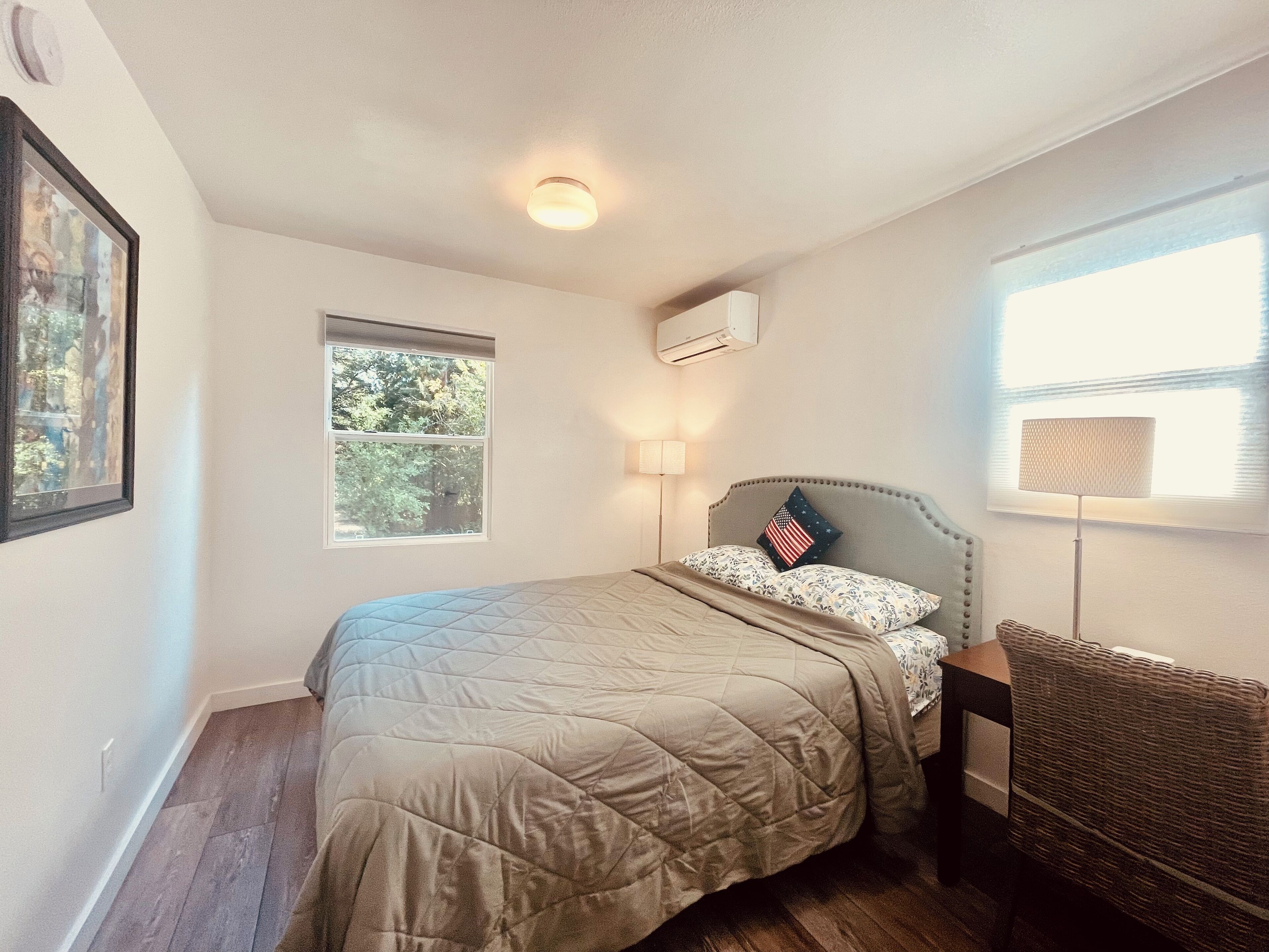 Un dormitorio con cama, ventana, aire acondicionado de pared y lámpara de pie.