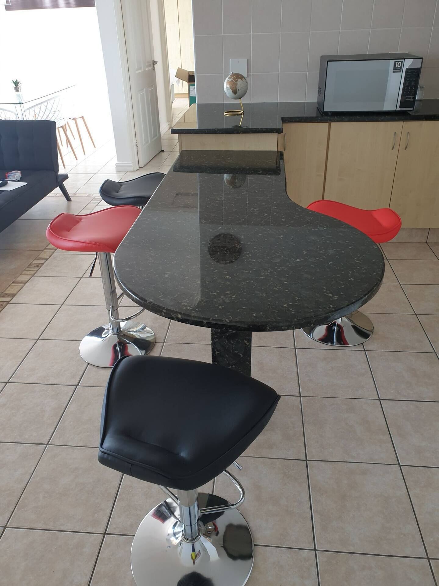 A kitchen with a round table, two red chairs, a black chair, and a microwave on the counter.