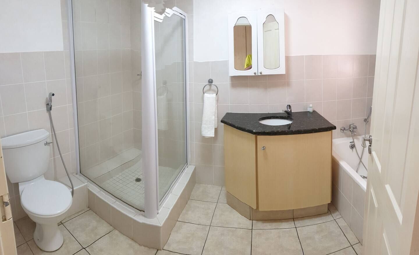 A bathroom with a glass-enclosed shower, a toilet, a sink with a black countertop, and a wooden cabinet.