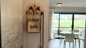 A hotel lobby with a wall-mounted decorative piece, a hanging bag with "hola" text, and a view of the outdoor patio area.