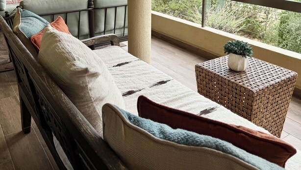 A balcony with a sofa, a small table with a plant, and a view of a golf course and buildings.