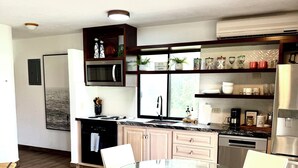 A modern kitchen with a glass dining table, white chairs, and wooden flooring.