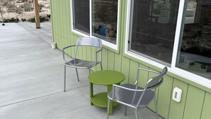 Un patio con dos sillas de metal y una mesa redonda pequeña, una ventana y suelo de concreto.