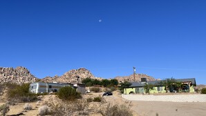 Paisaje desértico con colinas rocosas, una caravana y un pequeño edificio con techo verde.